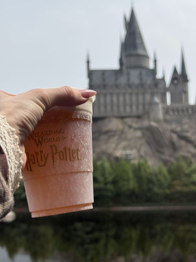 A butterbeer cup held up in front of Hogwarts castle at Universal Studios Beijing
