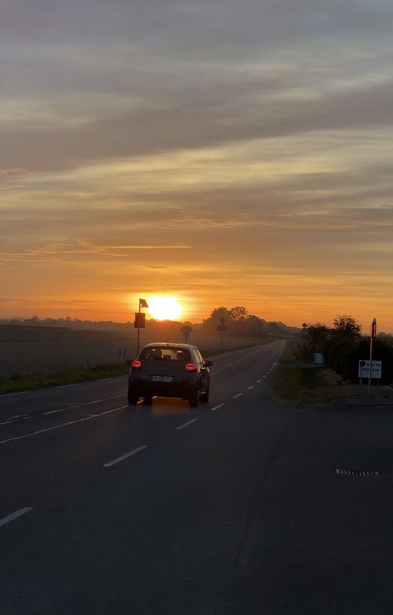 A car on an empty country road driving towards a bright orange sunrise