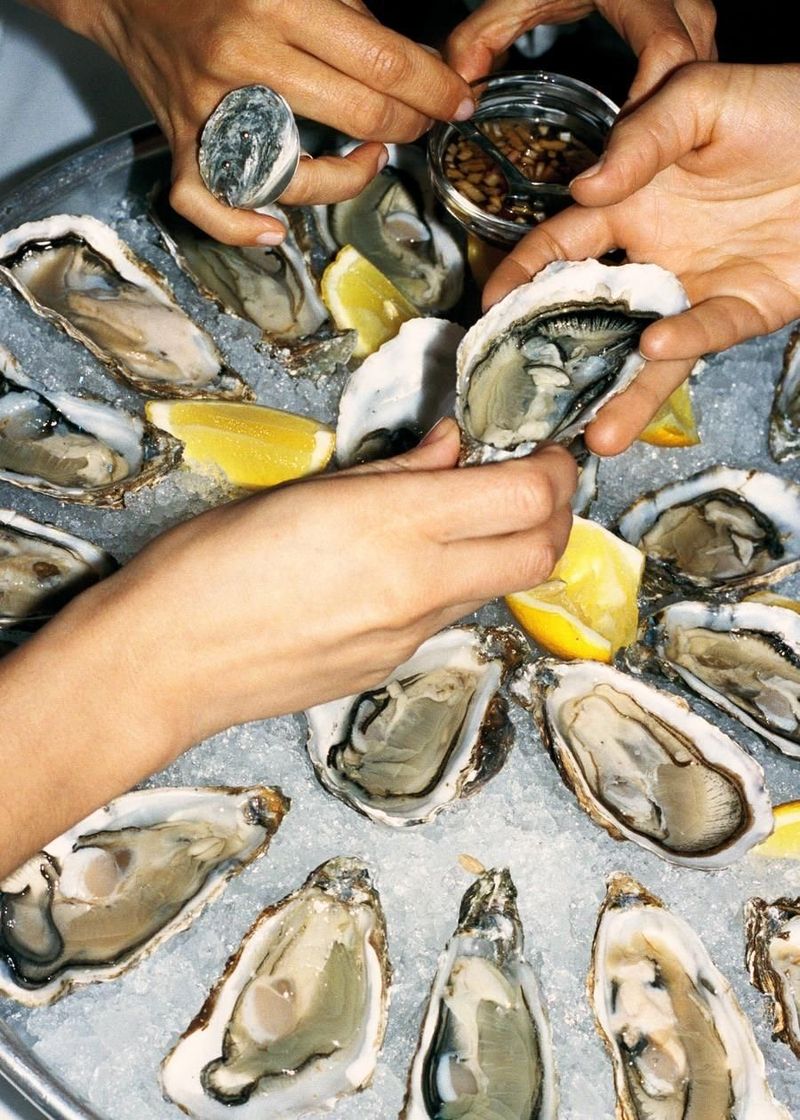 Hands reaching for fresh oysters on a bed of ice with lemon wedges