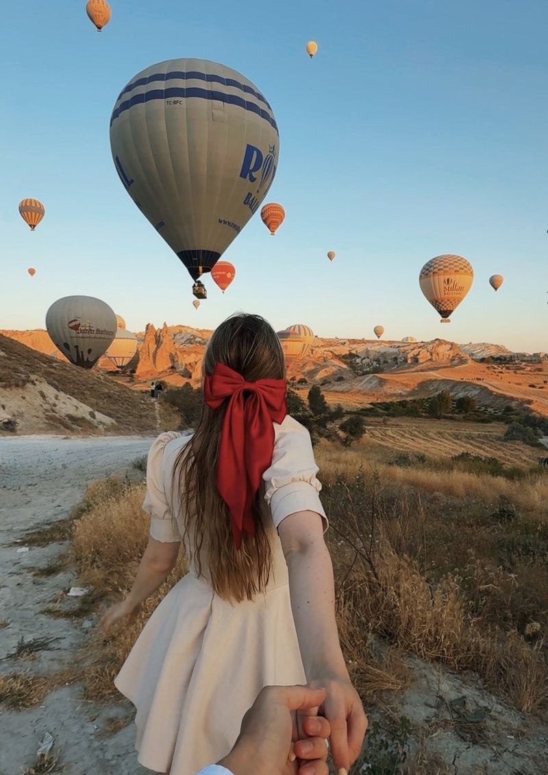 A girl with a big red bow in her hair leads the photographer by the hand towards a sky full of hot-air balloons over Cappadocia’s rocky valleys